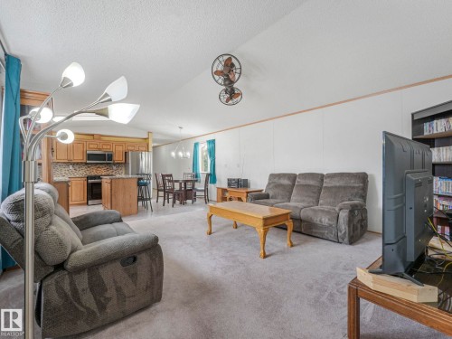 Open-concept living area with light-toned carpet flooring and white wall paneling - 151 3400 48 Street, Stony Plain, AB - Indoor