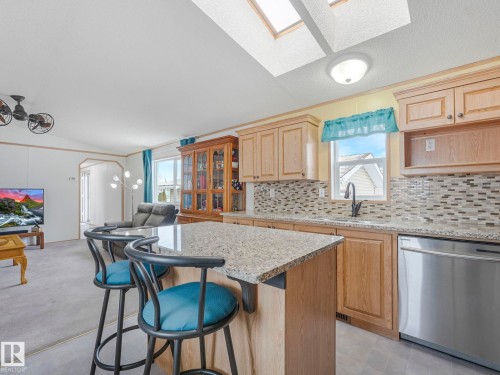 Kitchen island with granite countertop and integrated bar seating - 151 3400 48 Street, Stony Plain, AB - Indoor Photo Showing Other Room