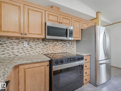 Kitchen featuring wood-finish cabinetry, stainless steel appliances, granite-style countertops, and a mosaic tile backsplash - 151 3400 48 Street, Stony Plain, AB - Indoor Photo Showing Kitchen