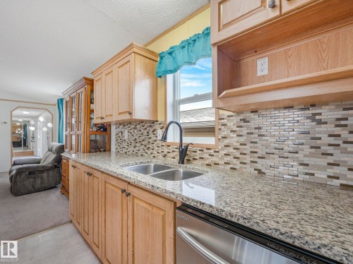 Kitchen featuring light wood cabinetry, granite-style countertops, a mosaic tile backsplash, and a double basin stainless steel sink with a black gooseneck faucet - 151 3400 48 Street, Stony Plain, AB - Indoor Photo Showing Kitchen With Double Sink