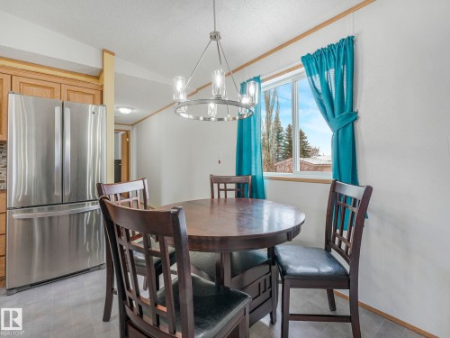 Dining area featuring a contemporary chandelier, wood-finish cabinetry, stainless steel French-door refrigerator, and a window with natural light - 151 3400 48 Street, Stony Plain, AB - Indoor Photo Showing Dining Room