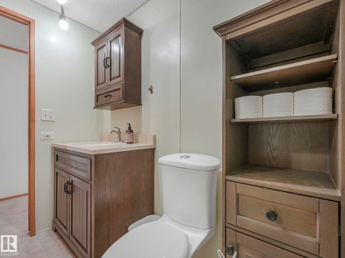 Bathroom featuring a white toilet, wood-finish vanity with a light-toned countertop, and an integrated sink - 151 3400 48 Street, Stony Plain, AB - Indoor Photo Showing Bathroom