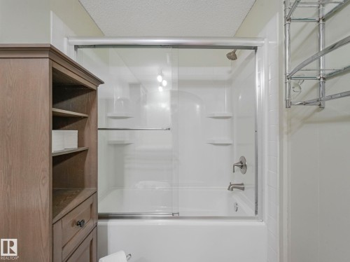 White tub-shower combination with sliding glass doors, chrome fixtures, and integrated shelving - 151 3400 48 Street, Stony Plain, AB - Indoor Photo Showing Bathroom