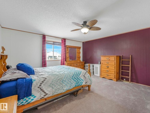 Carpeted room featuring a ceiling fan with integrated lighting, a window with horizontal blinds, and a deep plum accent wall with vertical paneling - 151 3400 48 Street, Stony Plain, AB - Indoor Photo Showing Bedroom