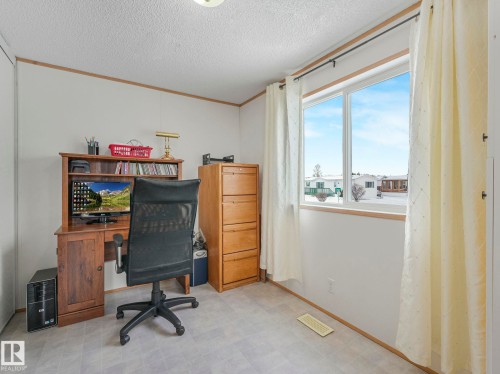 Bright room featuring a large window, light-colored walls, wood-finish trim, and textured flooring - 151 3400 48 Street, Stony Plain, AB - Indoor Photo Showing Office