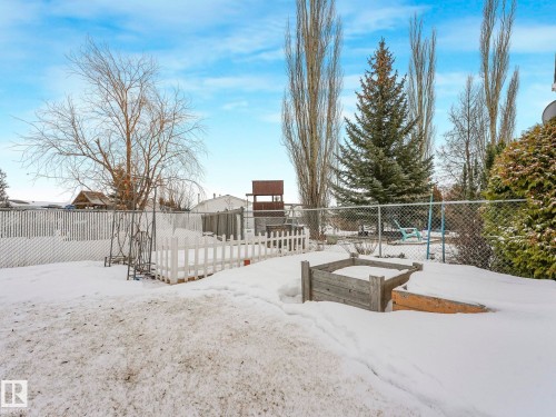 Expansive fenced backyard featuring a white picket fence, raised garden beds, mature trees, and a wooden play structure - 151 3400 48 Street, Stony Plain, AB - Outdoor