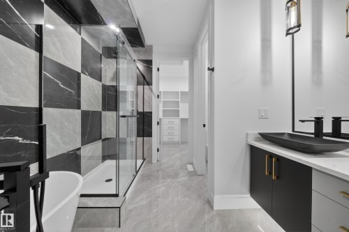 Contemporary bathroom featuring a freestanding soaking tub, a frameless glass shower enclosure with checkered tile surround, a single vanity with a vessel sink, and a walk-in closet with built-in shelving and drawers - 4005 39 Street, Beaumont, AB - Indoor Photo Showing Bathroom