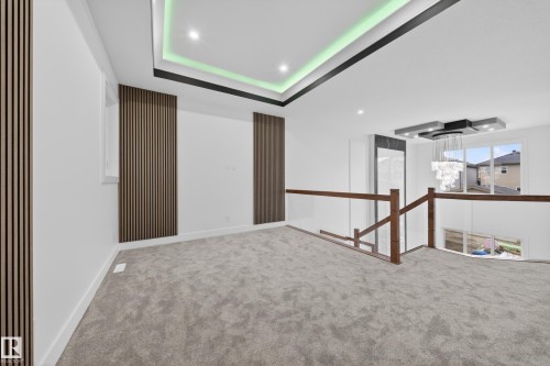 Spacious carpeted landing featuring wood-slat accent walls, a tray ceiling with integrated lighting, and a contemporary chandelier - 4005 39 Street, Beaumont, AB - Indoor Photo Showing Other Room