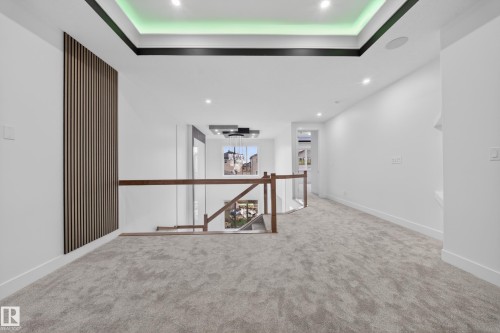 Upper-level landing featuring light gray carpeting, recessed ceiling lighting, a modern wood slat accent wall, and a staircase with a glass railing and wood handrail - 4005 39 Street, Beaumont, AB - Indoor Photo Showing Other Room