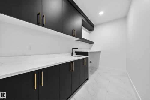 Laundry room featuring black flat-panel cabinetry with gold-tone hardware, white marble-look countertops, a black sink and faucet, and white tile flooring - 4005 39 Street, Beaumont, AB - Indoor