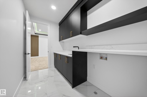 Utility space featuring large format white tile flooring, dark cabinetry with brass-finish hardware, white countertops, and a built-in sink with a black faucet - 4005 39 Street, Beaumont, AB - Indoor Photo Showing Other Room