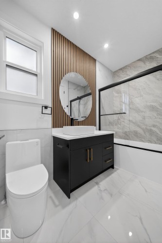 Modern bathroom featuring white tile flooring, a black vanity with gold-tone hardware, a vessel sink, and a circular mirror - 4005 39 Street, Beaumont, AB - Indoor Photo Showing Bathroom