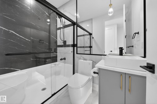 Modern bathroom featuring a glass-enclosed shower-tub combination with black marble-look wall tiling and a white basin - 4005 39 Street, Beaumont, AB - Indoor