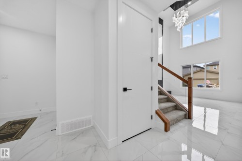 Two-story foyer featuring large windows, a contemporary chandelier, a carpeted staircase with wood handrails and glass panels, and polished tile flooring - 4005 39 Street, Beaumont, AB - Indoor Photo Showing Other Room