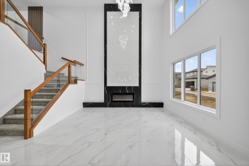 Two-story room featuring a floor-to-ceiling fireplace with black and white stone-finish surround, a contemporary electric firebox, and a decorative chandelier - 4005 39 Street, Beaumont, AB - Indoor Photo Showing Other Room