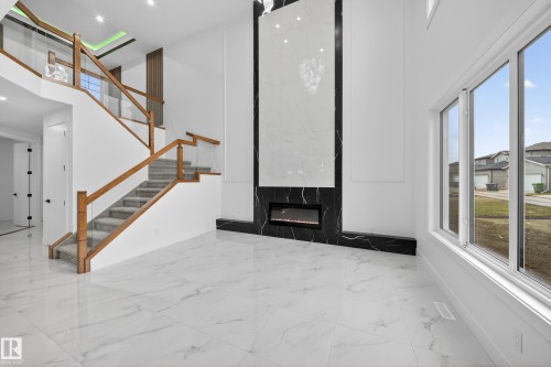 Two-story room featuring a modern fireplace with a black and white marble-finish surround, wood and glass staircase, large windows, and marble-finish tile flooring - 4005 39 Street, Beaumont, AB - Indoor Photo Showing Other Room