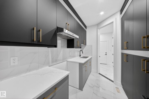 Contemporary kitchen featuring dark flat-panel cabinetry with gold-tone hardware, white marble-patterned countertops, and matching backsplash - 4005 39 Street, Beaumont, AB - Indoor Photo Showing Kitchen