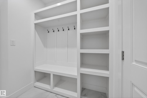 Built-in white storage unit featuring a bench, upper shelving, dark-toned coat hooks, and open lower storage compartments, set against a light-toned flooring - 4005 39 Street, Beaumont, AB - Indoor With Storage