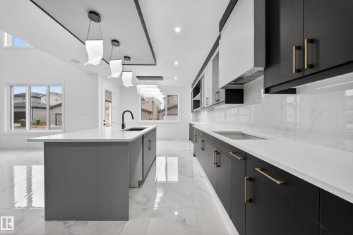 Contemporary kitchen featuring a large center island with integrated sink, white countertops, and a white and black cabinet combination with gold-tone hardware - 4005 39 Street, Beaumont, AB - Indoor Photo Showing Kitchen