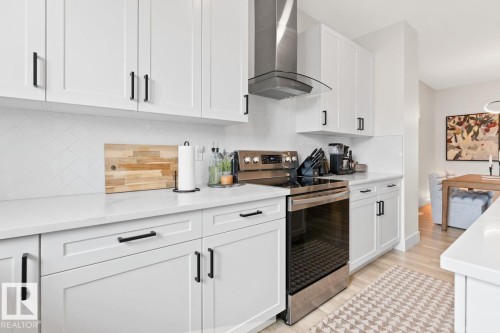 Modern kitchen featuring white shaker-style cabinetry, black hardware, white countertops, and a herringbone tile backsplash - 6023 180 Avenue, Edmonton, AB - Indoor Photo Showing Kitchen