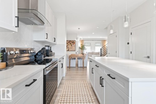Modern kitchen featuring white cabinetry, stainless steel appliances, a white tile backsplash, and a large central island - 6023 180 Avenue, Edmonton, AB - Indoor Photo Showing Kitchen With Upgraded Kitchen