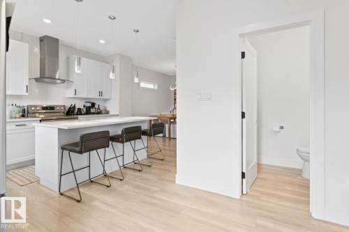 Kitchen featuring white cabinetry, a stainless steel range hood, and a central island with a light-toned countertop - 6023 180 Avenue, Edmonton, AB - Indoor Photo Showing Kitchen With Upgraded Kitchen