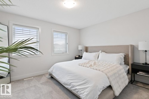 Carpeted bedroom featuring two windows with horizontal blinds, a neutral upholstered headboard, and a flush-mount ceiling light fixture - 6023 180 Avenue, Edmonton, AB - Indoor Photo Showing Bedroom