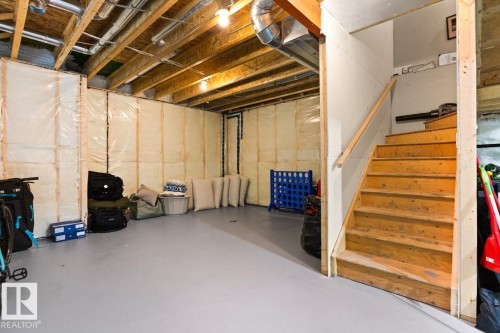Unfinished basement featuring exposed wood joists and structural elements, insulated wall sections, a painted concrete floor, and a wood staircase with a handrail - 6023 180 Avenue, Edmonton, AB - Indoor Photo Showing Basement
