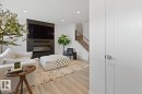Living area featuring a sleek fireplace with a black accent wall, light wood-finish flooring, recessed lighting, and a modern staircase with metal railings - 6023 180 Avenue, Edmonton, AB  - Indoor With Fireplace 