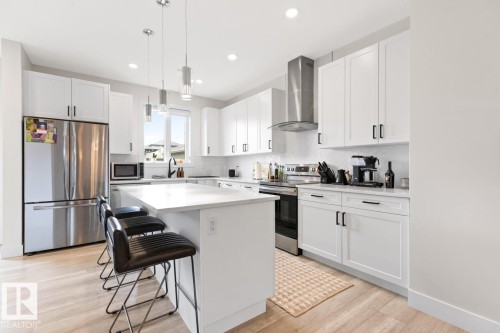 Modern kitchen featuring white shaker cabinetry, stainless steel appliances, a center island with seating, pendant lighting, and light wood-finish flooring - 6023 180 Avenue, Edmonton, AB - Indoor Photo Showing Kitchen With Stainless Steel Kitchen With Upgraded Kitchen