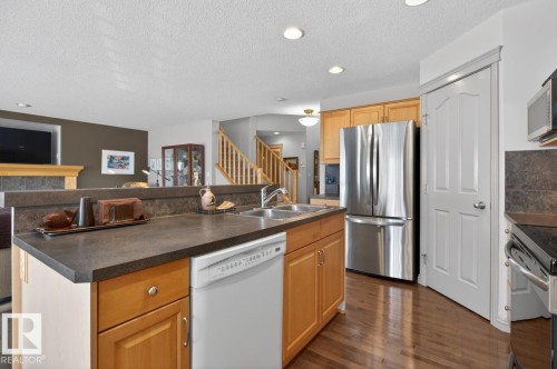 Kitchen featuring wood-finish flooring, light wood cabinetry, stainless steel refrigerator, white dishwasher, and dark countertops - 2178 Haddow Drive, Edmonton, AB - Indoor Photo Showing Kitchen With Double Sink