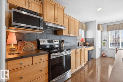 Kitchen featuring light wood cabinetry, dark countertops, and a full tile backsplash - 2178 Haddow Drive, Edmonton, AB - Indoor Photo Showing Kitchen