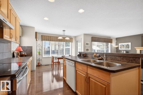 Kitchen featuring wood-finish cabinetry, dark countertops, and a tile backsplash - 2178 Haddow Drive, Edmonton, AB - Indoor Photo Showing Kitchen With Double Sink