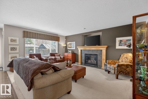 Living area featuring a natural wood fireplace mantel with stone surround, large windows with blinds, and a neutral carpet flooring - 2178 Haddow Drive, Edmonton, AB - Indoor Photo Showing Other Room With Fireplace