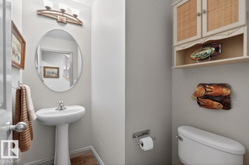 Pedestal sink with chrome faucet, an oval mirror, and a three-light vanity fixture - 2178 Haddow Drive, Edmonton, AB - Indoor Photo Showing Bathroom