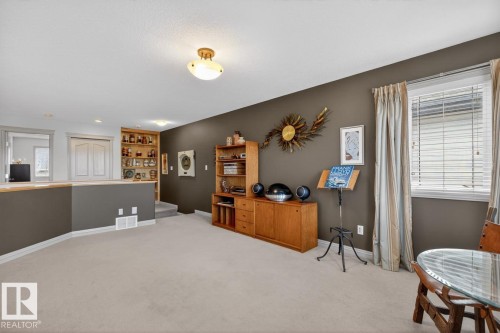Carpeted recreation room featuring an oak-finish media console, built-in shelving, a natural light window, and a recessed half-wall - 2178 Haddow Drive, Edmonton, AB - Indoor