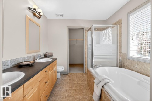 Bathroom featuring a spacious soaking tub, separate shower with glass enclosure, dual vanity with undermount sinks and dark countertops, light wood-finish cabinetry, and tiled flooring - 2178 Haddow Drive, Edmonton, AB - Indoor Photo Showing Bathroom