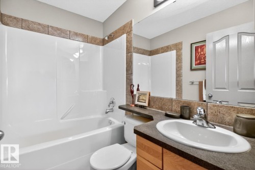 Bathroom featuring a white tub/shower combination, a vanity with a white oval sink, a dark countertop, wood-finish cabinetry, and a large wall-mounted mirror - 2178 Haddow Drive, Edmonton, AB - Indoor Photo Showing Bathroom