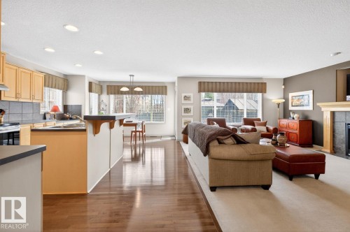 Open-concept living space featuring wood-finish flooring, recessed lighting, and a kitchen with light wood cabinetry and dark tile backsplash - 2178 Haddow Drive, Edmonton, AB - Indoor With Fireplace