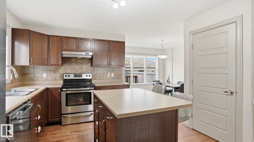 Kitchen featuring wood-finish flooring, dark wood cabinetry, stainless steel appliances, and a central island with a light-toned countertop - 8210 180 Avenue Nw, Edmonton, AB - Indoor Photo Showing Kitchen With Double Sink