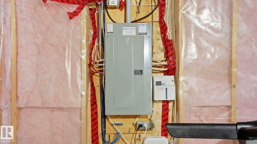 Electrical panel with exposed wiring, wood framing, and pink insulation with vapor barrier - 8210 180 Avenue Nw, Edmonton, AB - Indoor Photo Showing Basement