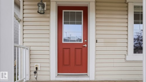 Entryway featuring a red door with upper window panes, framed by cream-colored horizontal siding - 8210 180 Avenue Nw, Edmonton, AB - Outdoor With Exterior