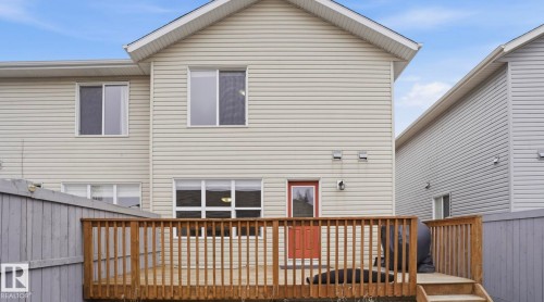 Rear exterior featuring light-colored horizontal siding, a wooden deck, and a contrasting red exterior door - 8210 180 Avenue Nw, Edmonton, AB - Outdoor With Deck Patio Veranda With Exterior