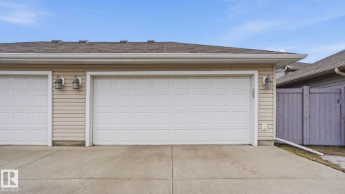 Two white panel garage doors with exterior lighting, beige horizontal siding, and a concrete driveway - 8210 180 Avenue Nw, Edmonton, AB - Outdoor With Exterior