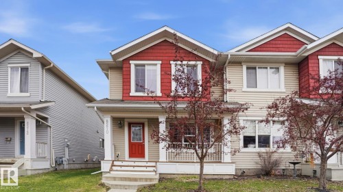 Two-story residence featuring a covered front porch with white columns, a red entry door with glass inserts, and a contrasting red and beige siding facade - 8210 180 Avenue Nw, Edmonton, AB - Outdoor With Facade