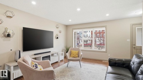 Living area featuring light neutral wall tones, recessed lighting, wood-finish flooring, a large window, and a built-in media console - 8210 180 Avenue Nw, Edmonton, AB - Indoor Photo Showing Living Room