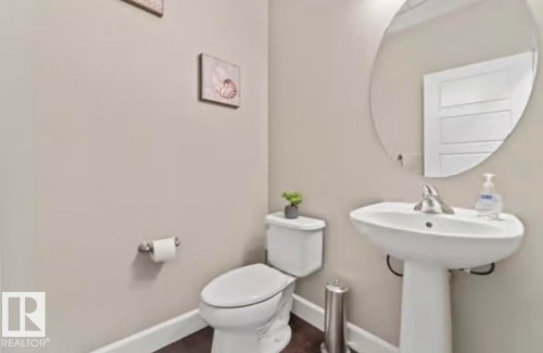 Pedestal sink with chrome faucet, complemented by a large circular mirror - 1944 67 Street, Edmonton, AB - Indoor Photo Showing Bathroom