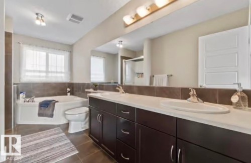 Bathroom featuring a large vanity with dual sinks, dark wood-finish cabinetry, and a spacious built-in tub with tile surround - 1944 67 Street, Edmonton, AB - Indoor Photo Showing Bathroom