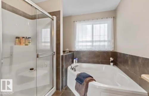 Shower enclosure with a clear glass door and an integrated corner tub featuring brown wall tile surround and a window with sheer coverings - 1944 67 Street, Edmonton, AB - Indoor Photo Showing Bathroom