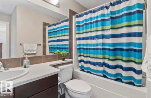 Bathroom featuring a white bathtub with an integrated shower, a white toilet, and a vanity with a dark wood-finish base and a white countertop - 1944 67 Street, Edmonton, AB - Indoor Photo Showing Bathroom